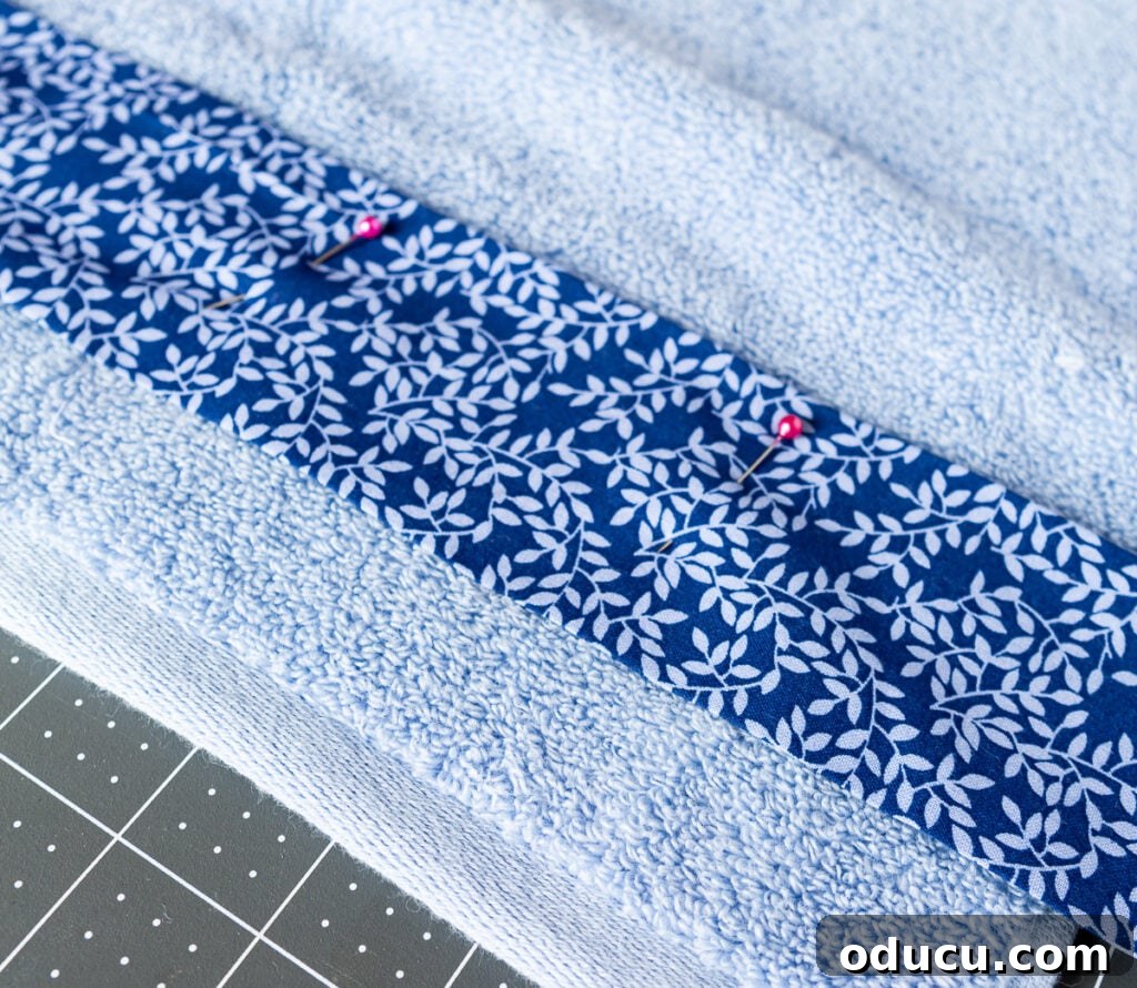 Elevate Your Bathroom With Towel Decor 16 Detailed image showing a vibrant blue fabric strip being carefully pinned to a bath towel, demonstrating precise placement before it is sewn into place.
