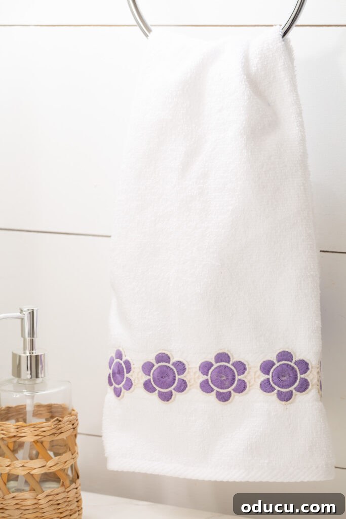 Elevate Your Bathroom With Towel Decor 17 A beautifully decorated hand towel with vintage purple and white flower ribbon sewn onto it, hanging gracefully from a towel ring in a pristine bathroom.