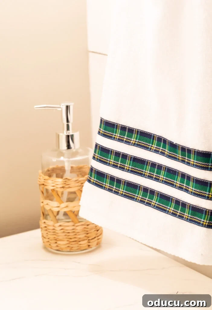 Elevate Your Bathroom With Towel Decor 20 A pristine white hand towel is adorned with three artfully arranged rows of blue and yellow plaid ribbon, creating a vibrant decorative detail. It hangs elegantly on a chrome towel ring in a modern bathroom.