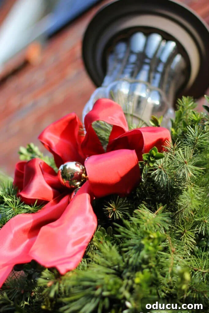 Outdoor light fixture on house with a red bow and greenery.