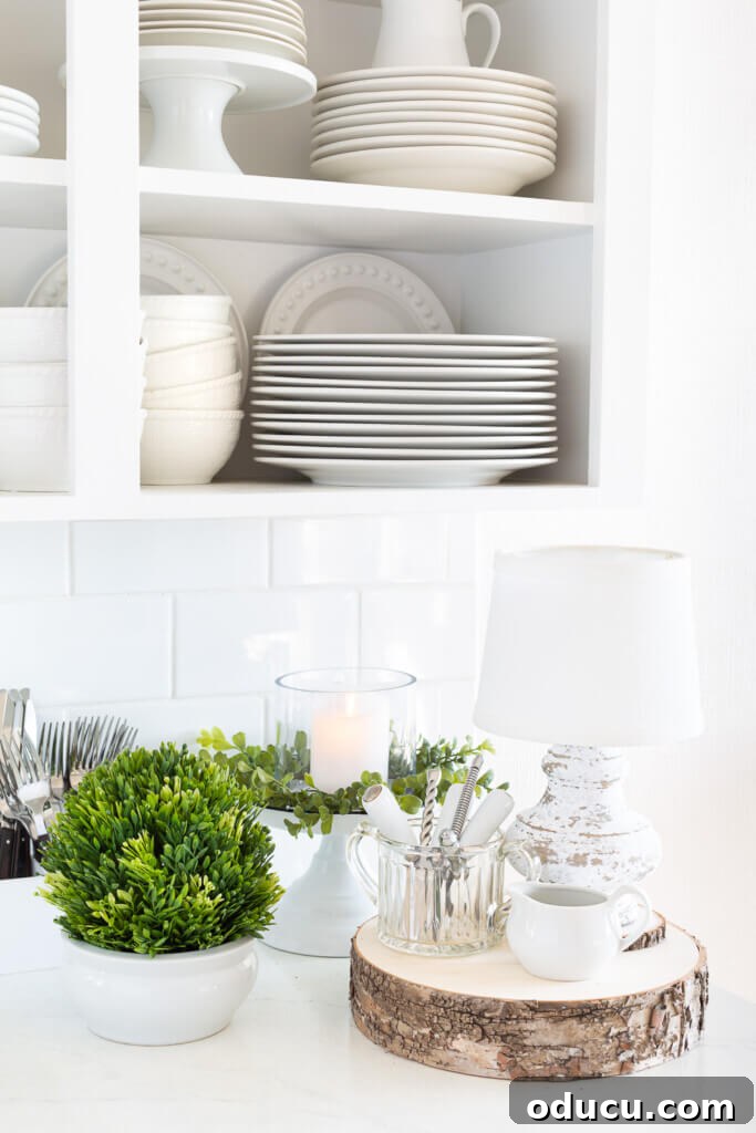 Mastering Ambiance A Decorator's Guide to Perfect Lighting 15 After Christmas decorating ideas for the kitchen. White kitchen with greenery and white plates and dishes on a counter.