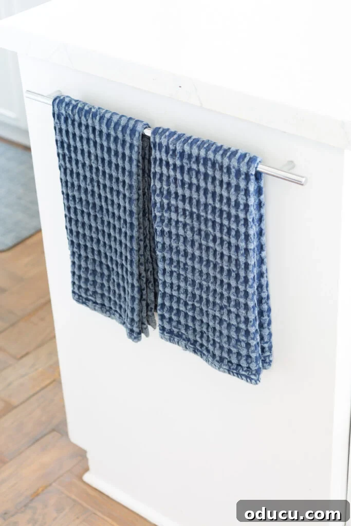 Blue waffle weave dish towels hanging neatly on a towel rack in a kitchen.