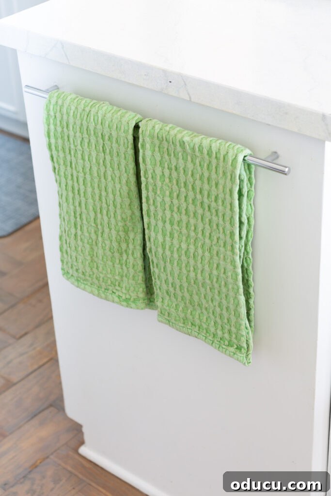 Spring green waffle weave dish towels hanging on a towel bar in a kitchen.