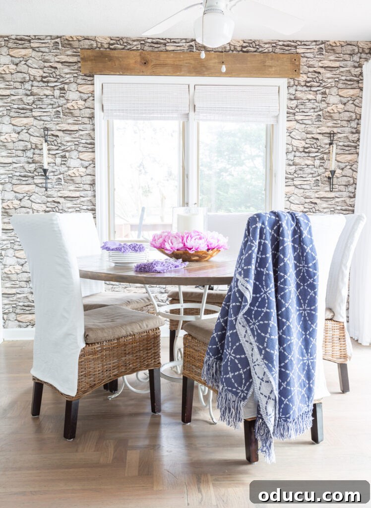 Blue and white throw blanket draped over a white slipcovered kitchen chair around a dining table.