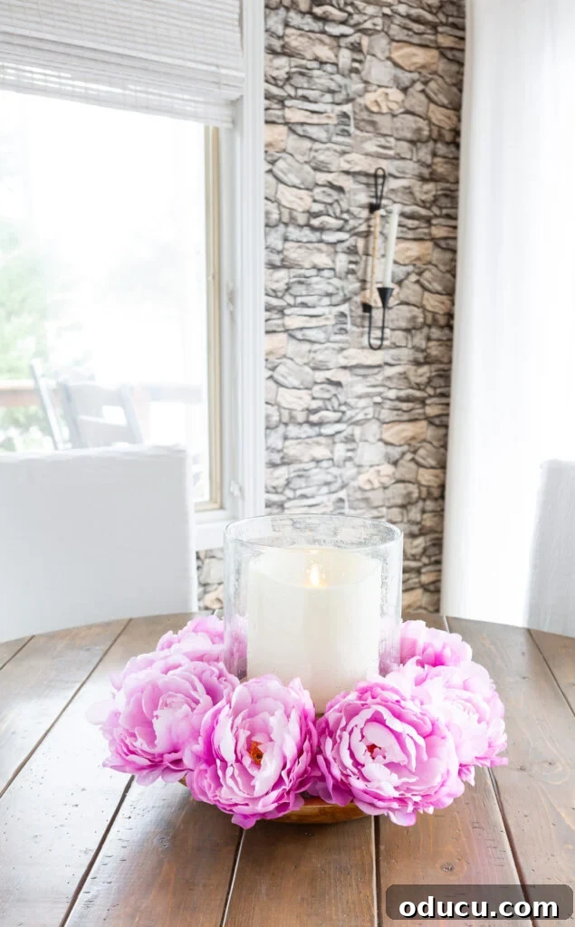 Pink floral table centerpiece with a large candle in a wooden bowl.