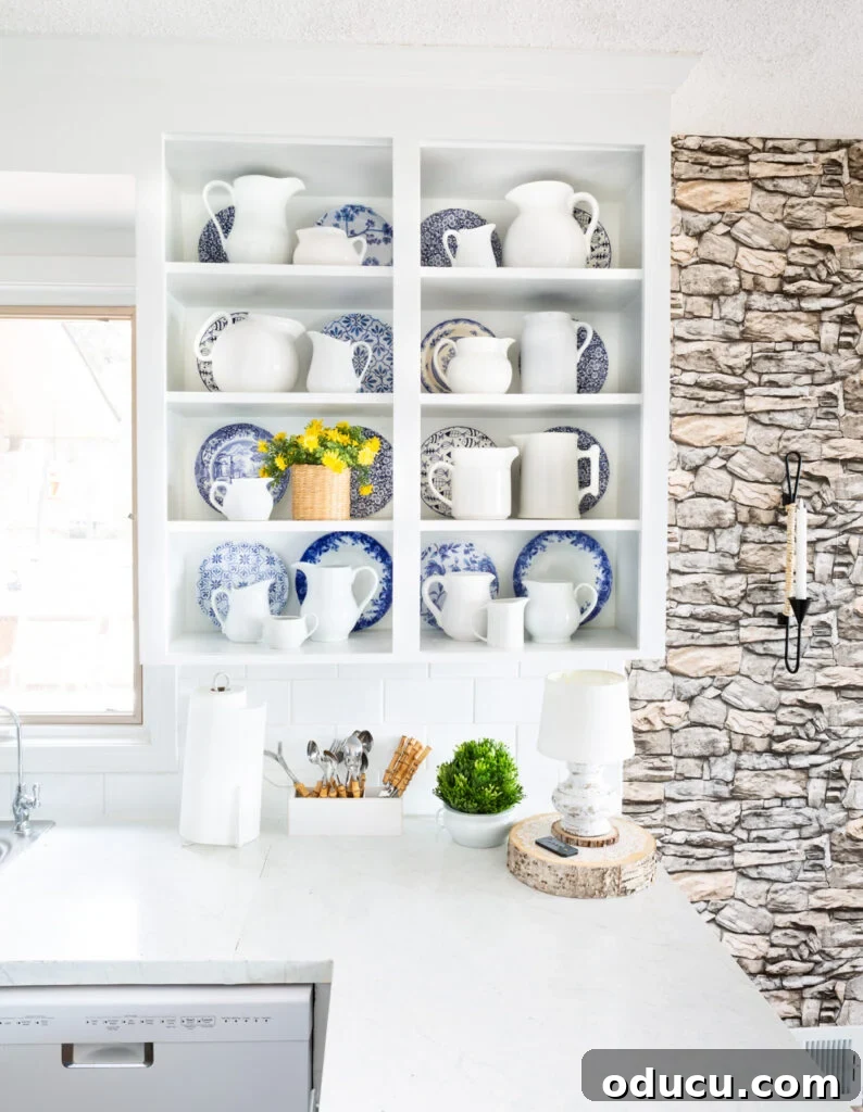 Neutral white kitchen with stone wall and white and blue accent decor on open shelves.