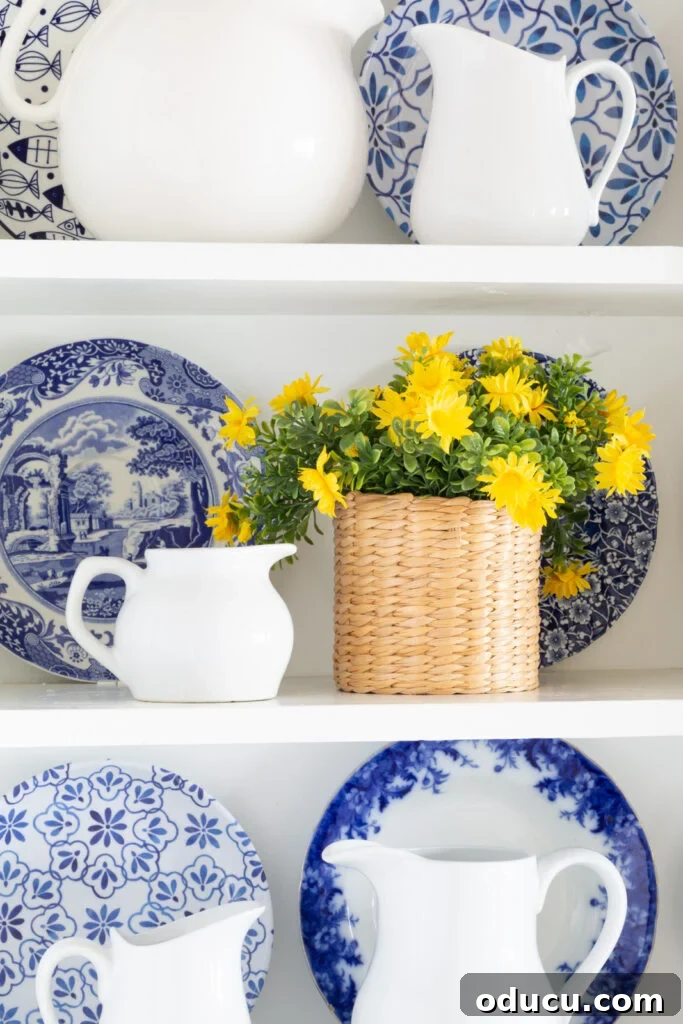 Spring flowers in a wicker vase displayed on open shelves in a white kitchen, adding a pop of yellow.