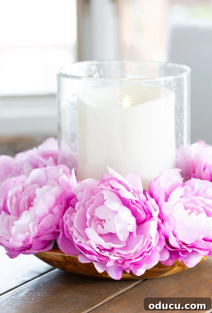 Mastering Faux Florals: Top 12 Decorating Secrets 13 Pink flowers surrounding a large candle that is placed in a large bowl on a wood table.