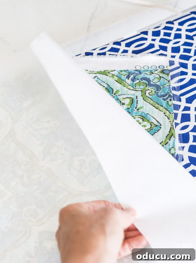 From Neglected Stool to Elegant Ottoman 12 Peeling Heat n Bond vinyl from its backing paper before application to fabric, showing the clear vinyl layer.