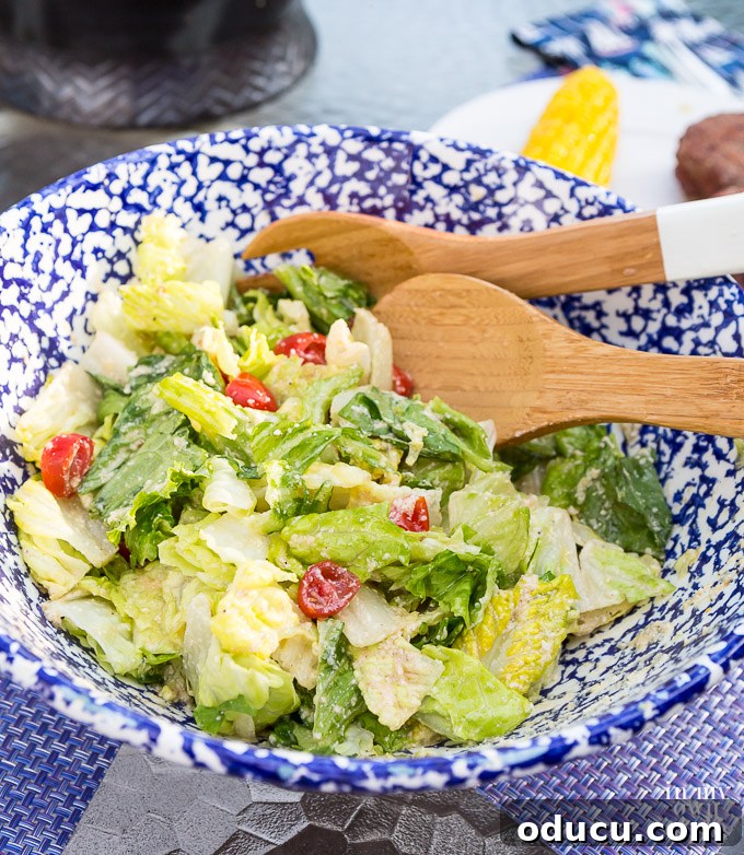 The Ultimate Anchovy-Free Caesar Salad 12 Caesar Salad in blue and white speckled bowl with wooden spoon and fork ready to be served.