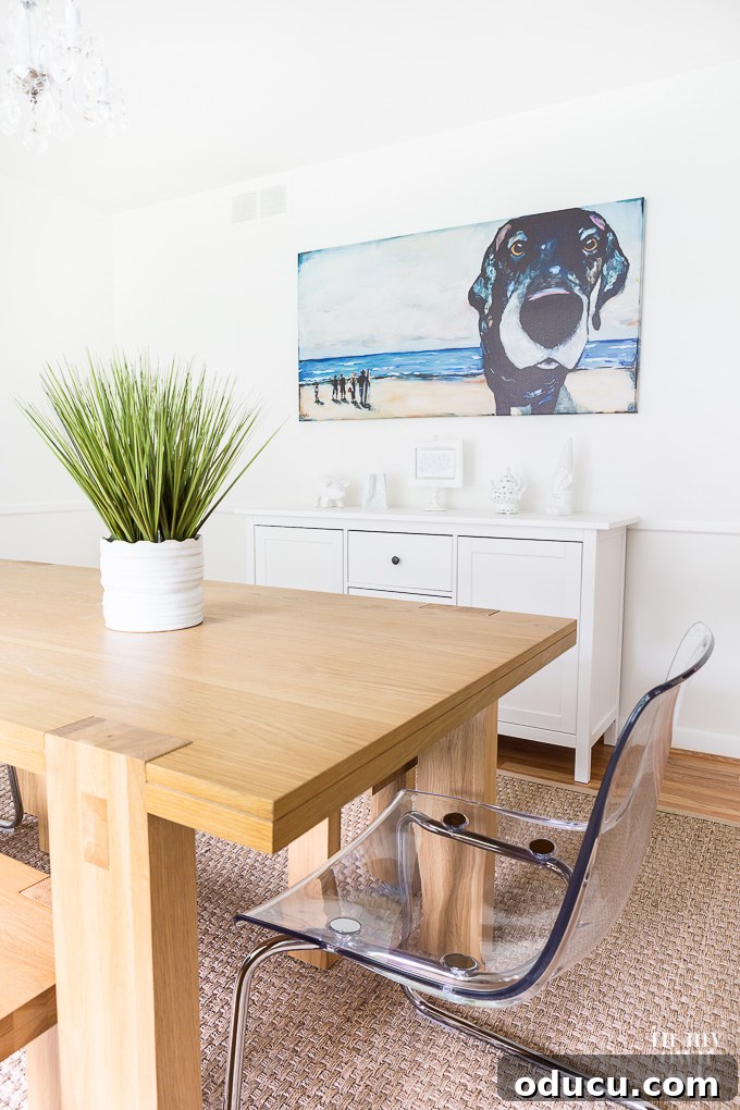 A newly renovated dining room featuring a modern table, ghost chairs, and an oversized dog art print on the wall, creating an inviting space.