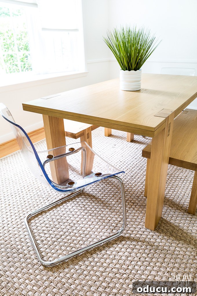 A modern dining room with a West Elm table and bench atop a seagrass rug, complemented by transparent ghost chairs.