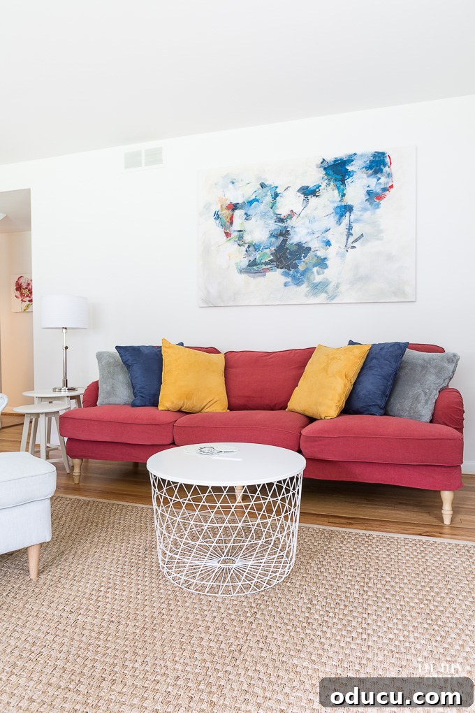 A vibrant red sofa from IKEA adds a bold pop of color to the otherwise white and neutral living room.