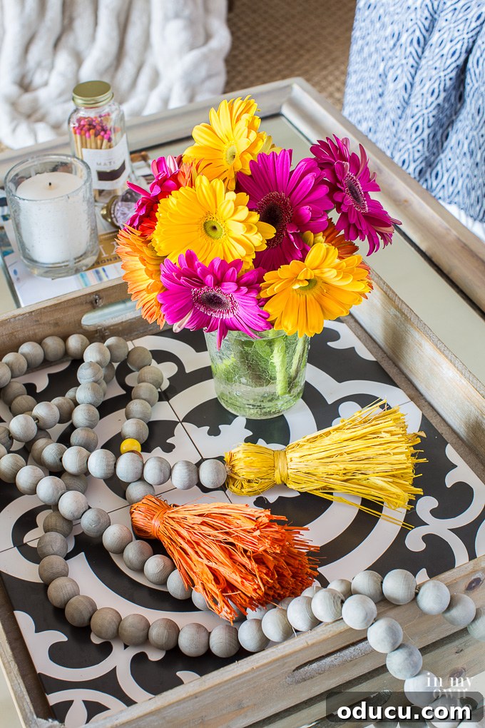 Coffee table tray styling ideas for colorful fall decorating using a trendy tile base. Fall styled coffee table tray with yellow and fuschia flowers and a driftwood bead garland
