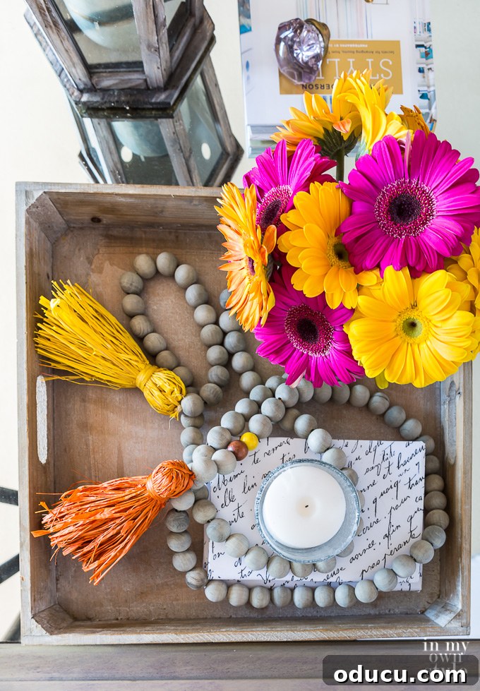 How to style a coffee table tray for fall with flowers, candles and a wood bead garland. Wood tray decorated for fall with vibrant flowers and wood bead garland before tile addition