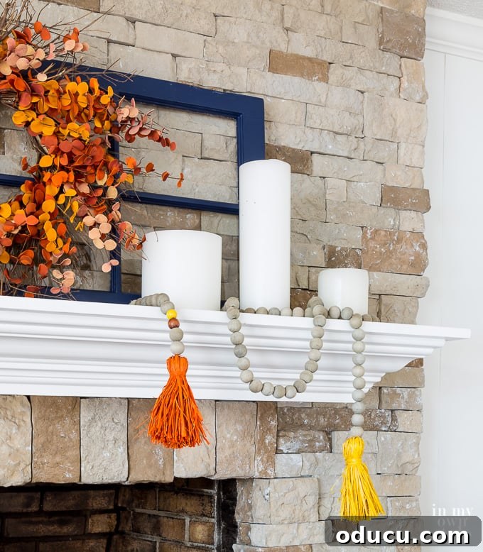 DIY Driftwood Wood Bead Garland with Colorful Raffia Tassels for Autumn Decor A beautifully styled fireplace mantel featuring a handcrafted driftwood wood bead garland with colorful raffia tassels, perfect for fall decorating.