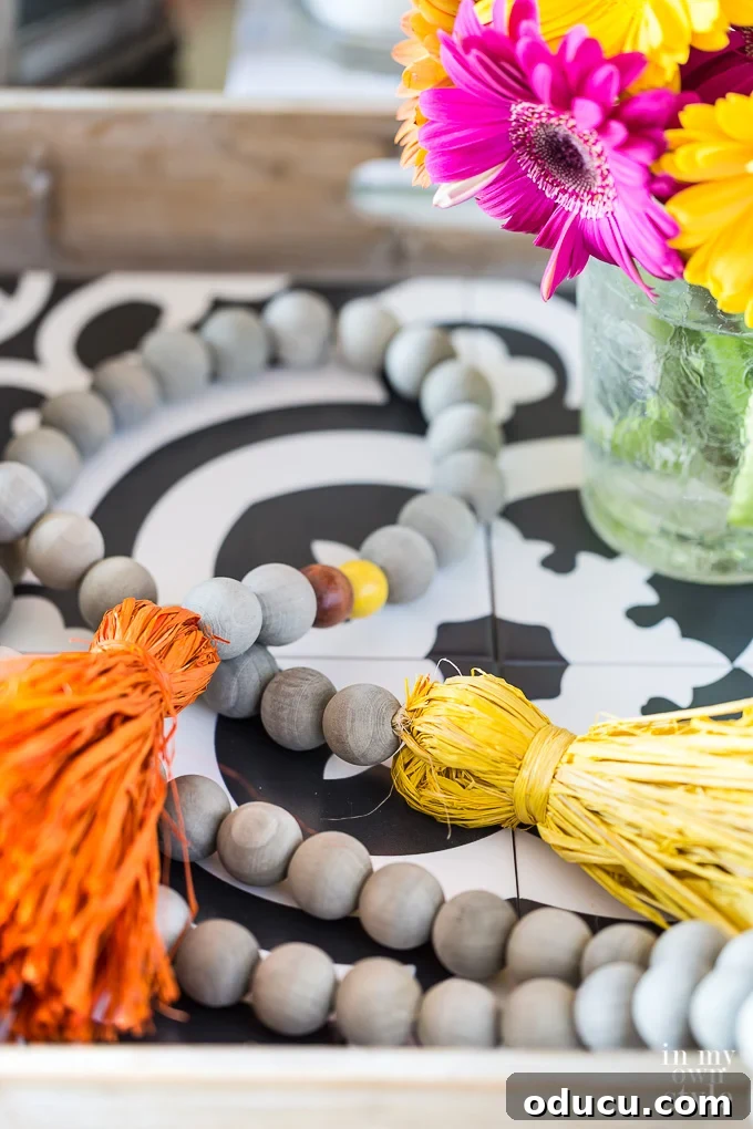 Styling a Wood Bead Driftwood Garland with Fall Raffia Tassels on a Tray A stylish coffee table tray adorned with a driftwood stained wood bead garland and fall-inspired colorful raffia tassels, demonstrating elegant autumn styling.