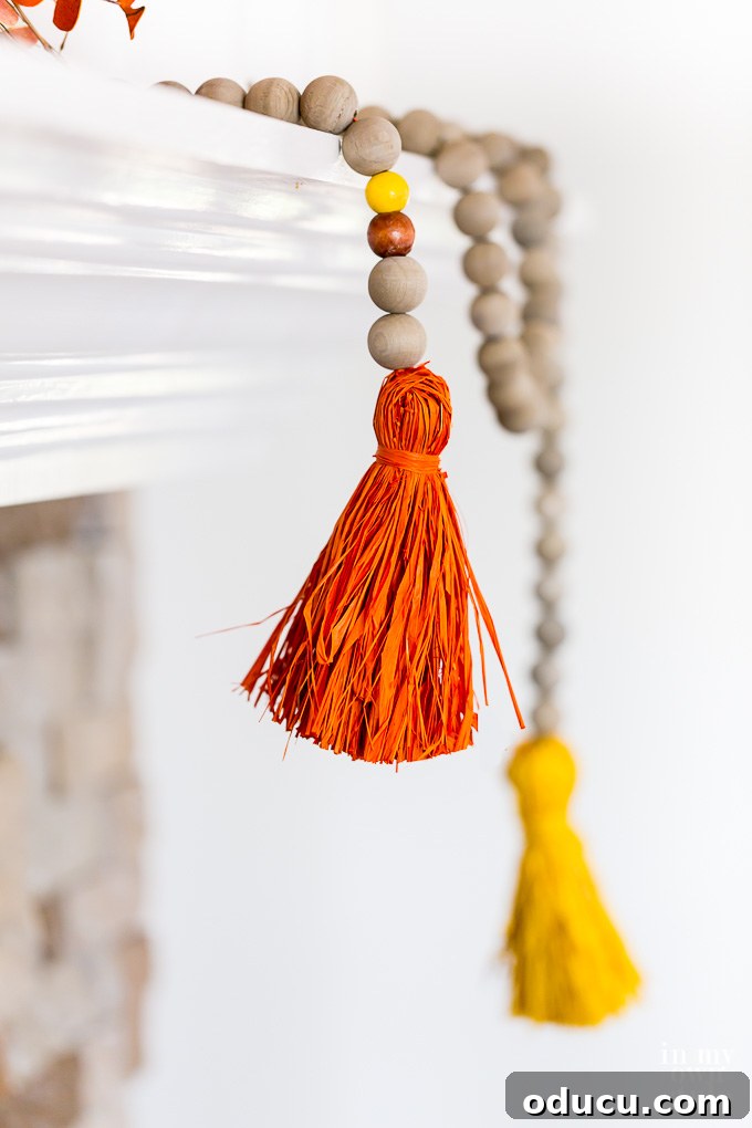 How to decorate a fall mantel using a wood bead garland. Close up shot of a rustic wood bead garland with raffia tassels draped off a mantel decorated for fall.
