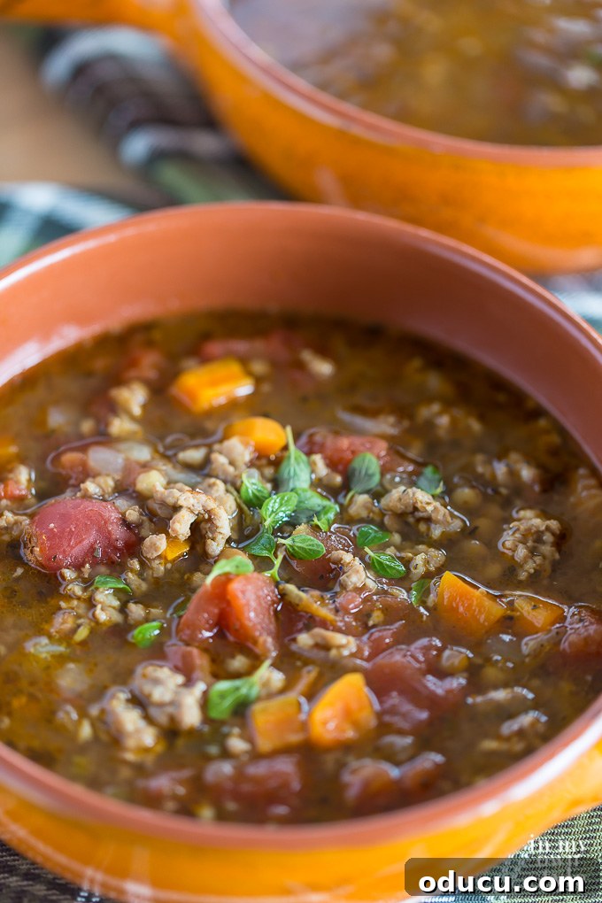 Close up shot of Sausage and Lentil Soup in an orange bowl, highlighting texture and ingredients.