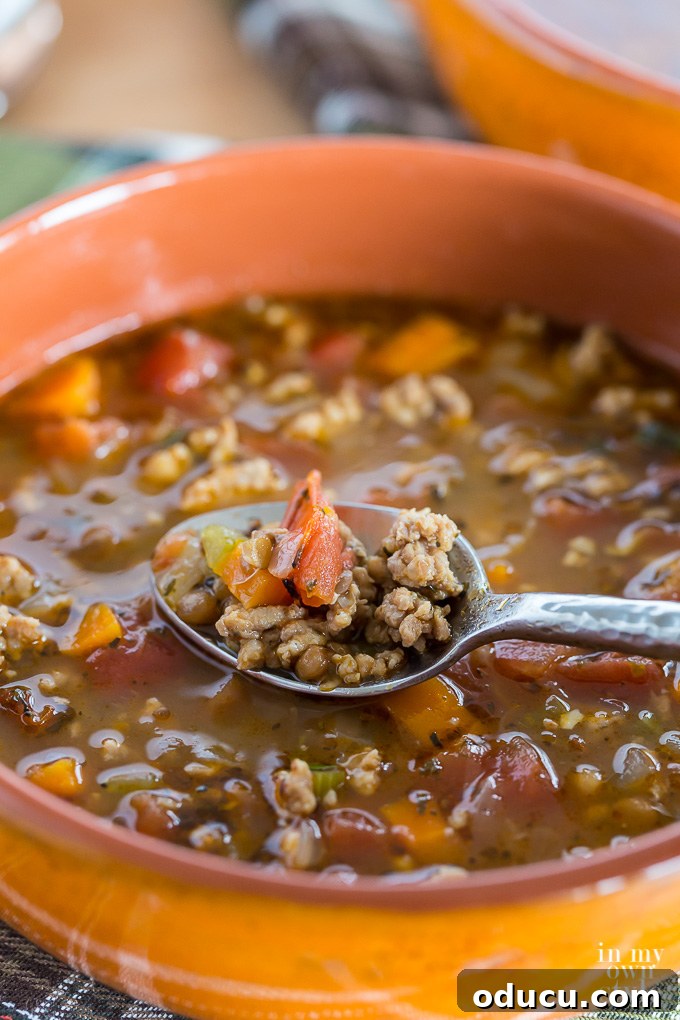 Sausage and lentil soup being spooned out of a soup bowl, indicating its hearty texture.