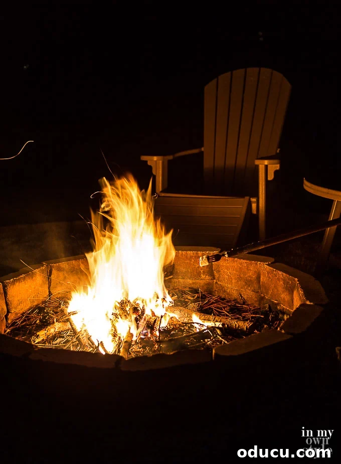 Outdoor Fire Pit Ready for S'Mores with DIY Marshmallow Roasting Sticks – Enjoy Campfire Cooking at Home An inviting outdoor fire pit, set up and ready for an evening of s'mores. Several DIY marshmallow roasting sticks, complete with forks, are visible, highlighting easy homemade solutions for campfire cooking fun.