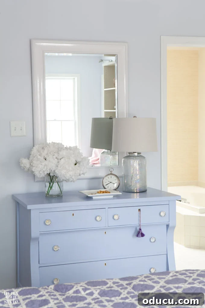 glossy white paint on mirror above blue dresser in bedroom that helps to brighten a dark room A mirror with glossy white paint frame, positioned above a blue dresser in a bedroom, effectively brightening a dark room.