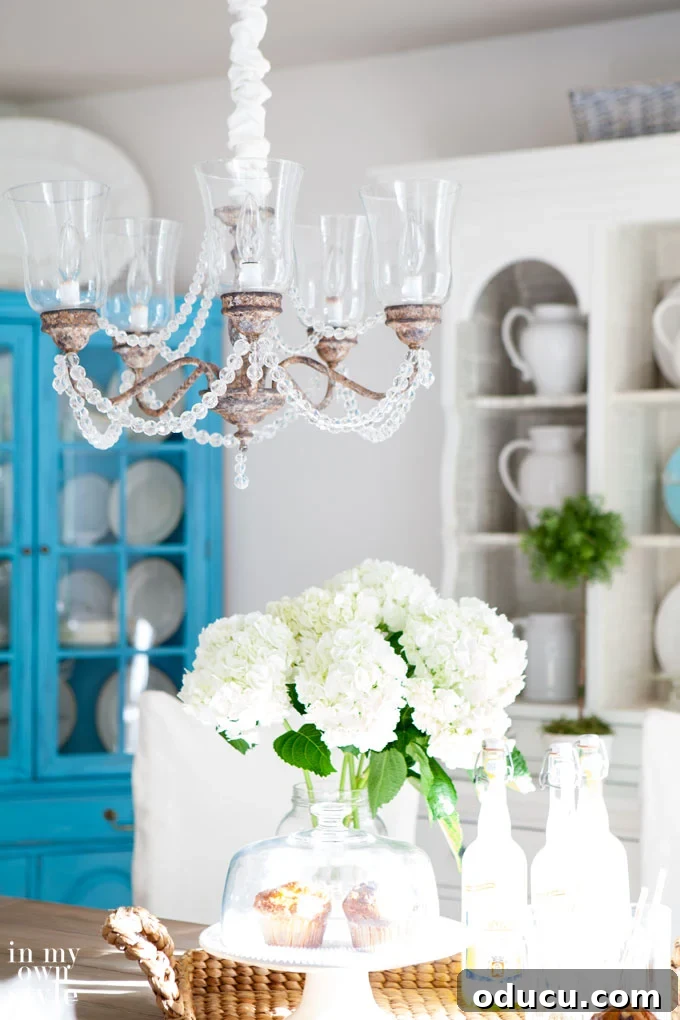 8 tips and tricks that will show you how to brighten a dark room in your home. Some can be done in minutes, others might take a day, but all of them will remove dark a drab from any room. Even one without natural light. #roomlighting #lightingtips #darkrooms #lamps #whiterooms #northfacingroompaint Brightly painted chairs and a chandelier with glass globes and crystals contributing to a bright dining room, showcasing effective ways to lighten a dark room.