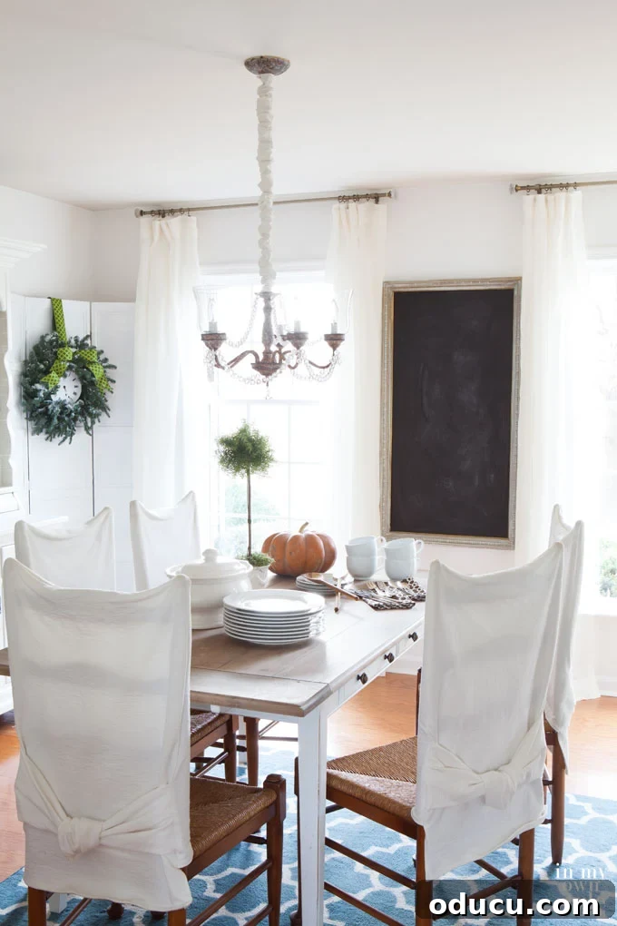 How should I hang drapes if I want to brighten a dark room? Elegant dining room featuring white drapes and a chalk-painted table, showcasing optimal window dressing for maximum light.