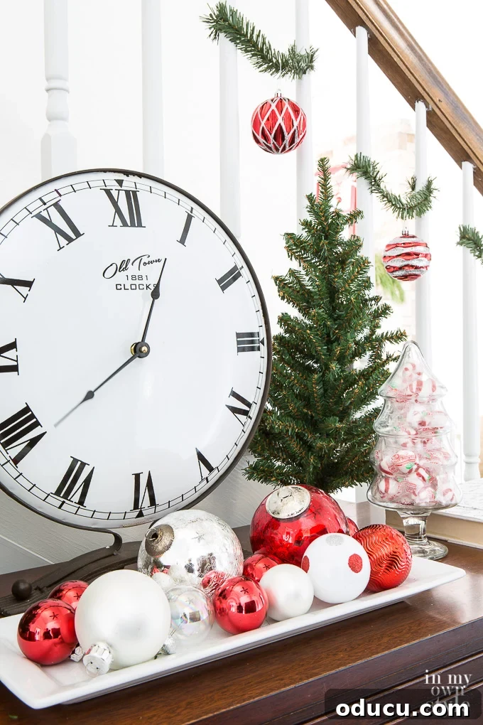 Tips for Simplifying Christmas Decorating A charming table clock sits amidst simple white, red, and green Christmas decorations, symbolizing a focus on time and meaningful moments over elaborate display.