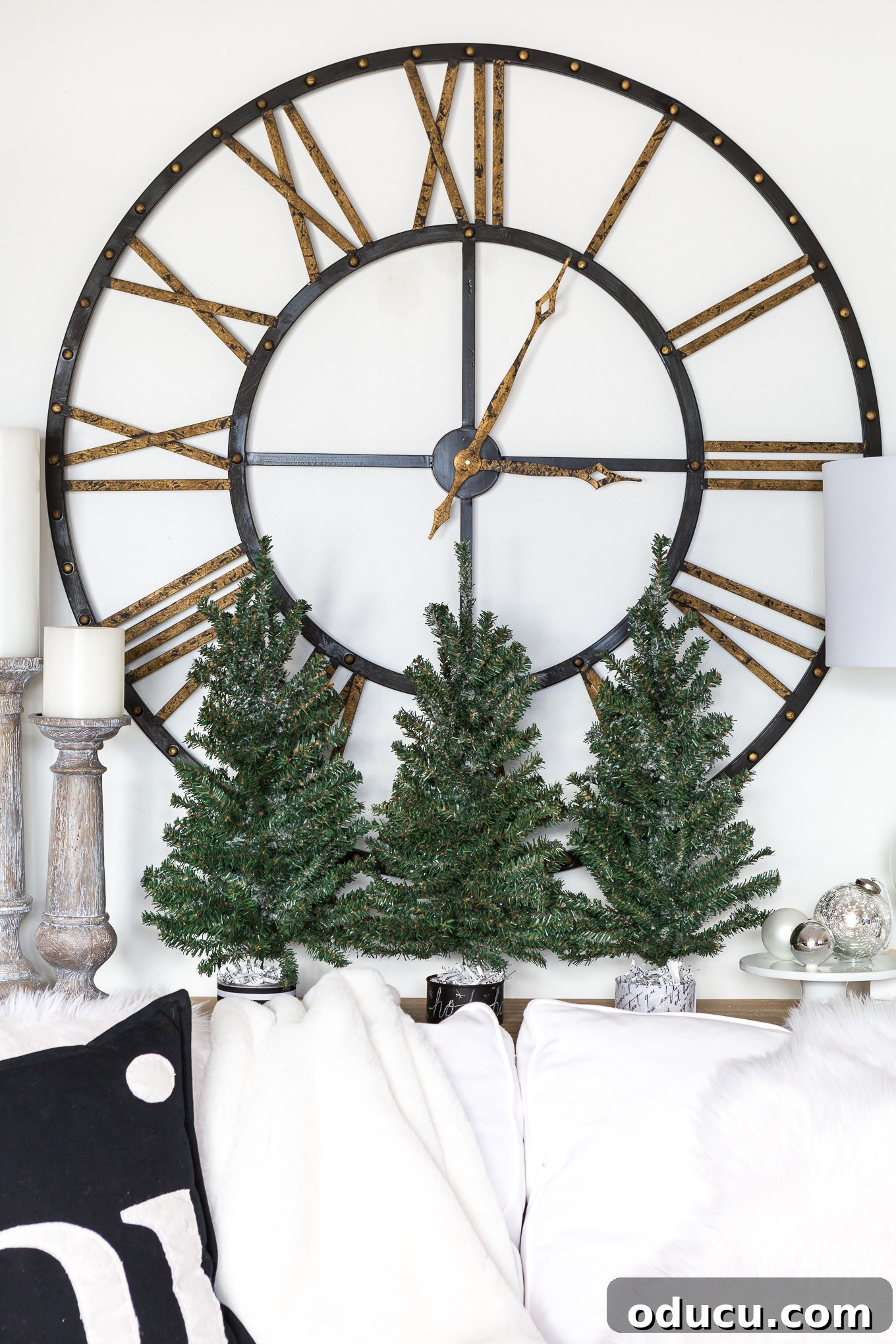 Living room Christmas decor. 3 pine trees on sofa table with a large metal clock behind it. 3 pine trees on sofa table with a large metal clock behind it, blending modern and rustic