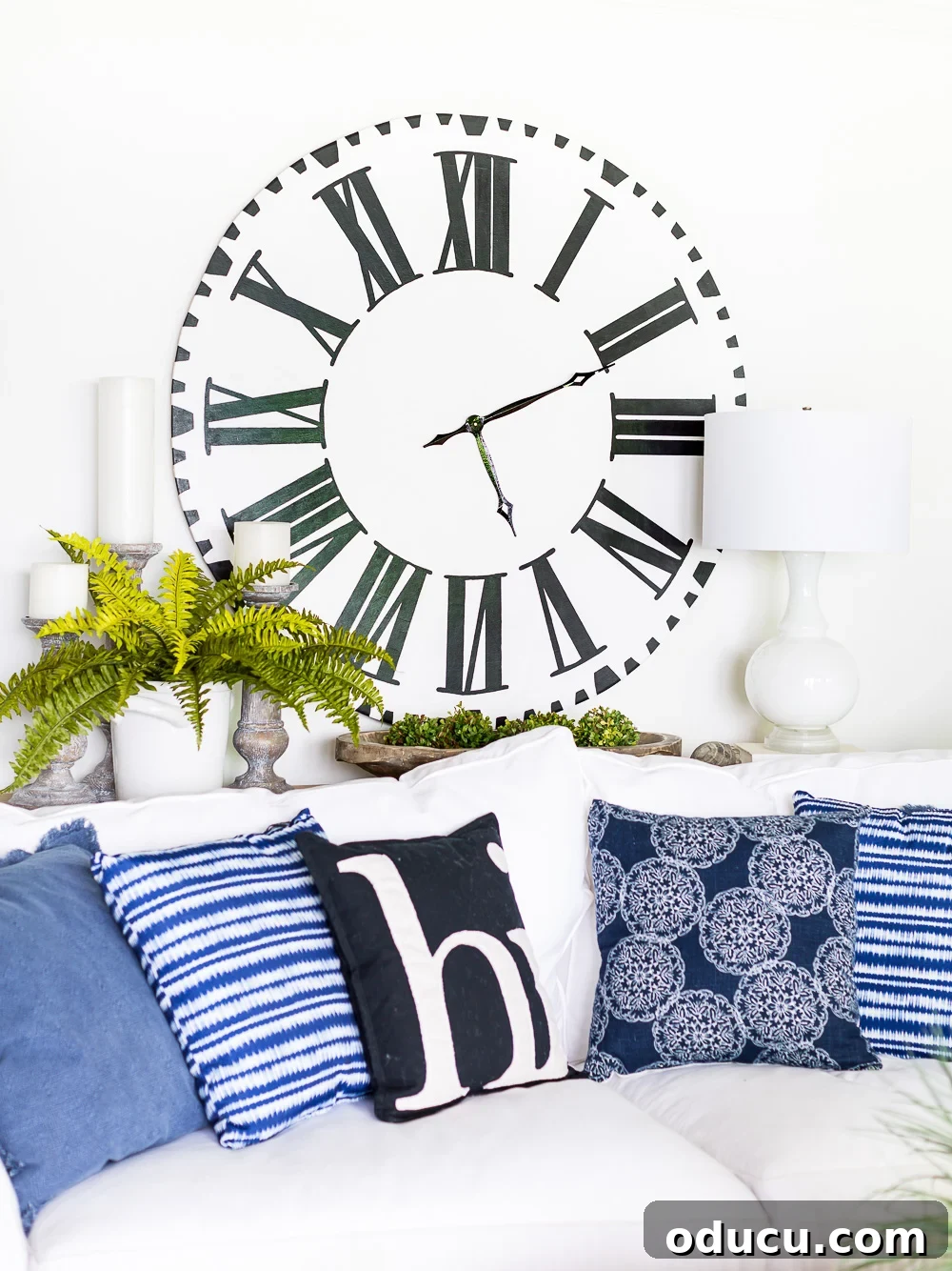 DIY Giant Farmhouse Wall Clock 18 An elegant white-faced Roman numeral oversized clock graces a wall in a beautifully decorated blue and white living room, showcasing a harmonious blend of styles.