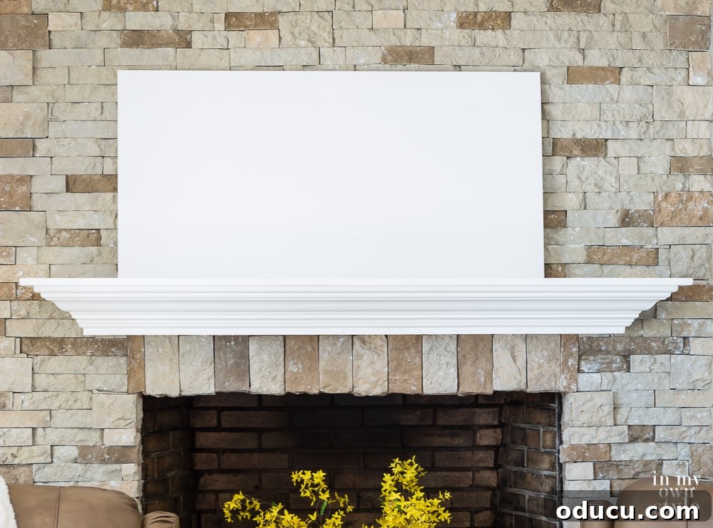 Start decorating a mantel by placing the largest item or layer first. The initial step of mantel decoration, featuring a large, flat white canvas placed off-center against the fireplace wall, establishing the first layer.