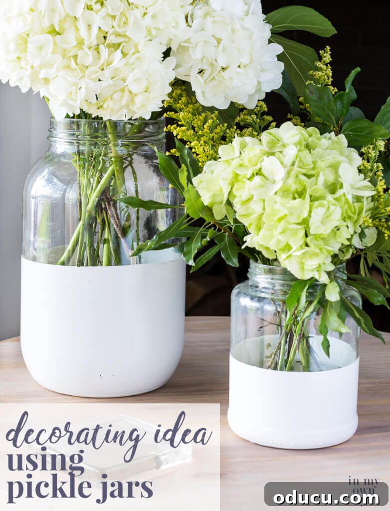 Craft a Stunning Oversized Glass Candle Lantern 11 Two glass pickle jars transformed into chic vases by dipping them in white paint. The text overlay suggests 'Decorating Idea using pickle jars.'