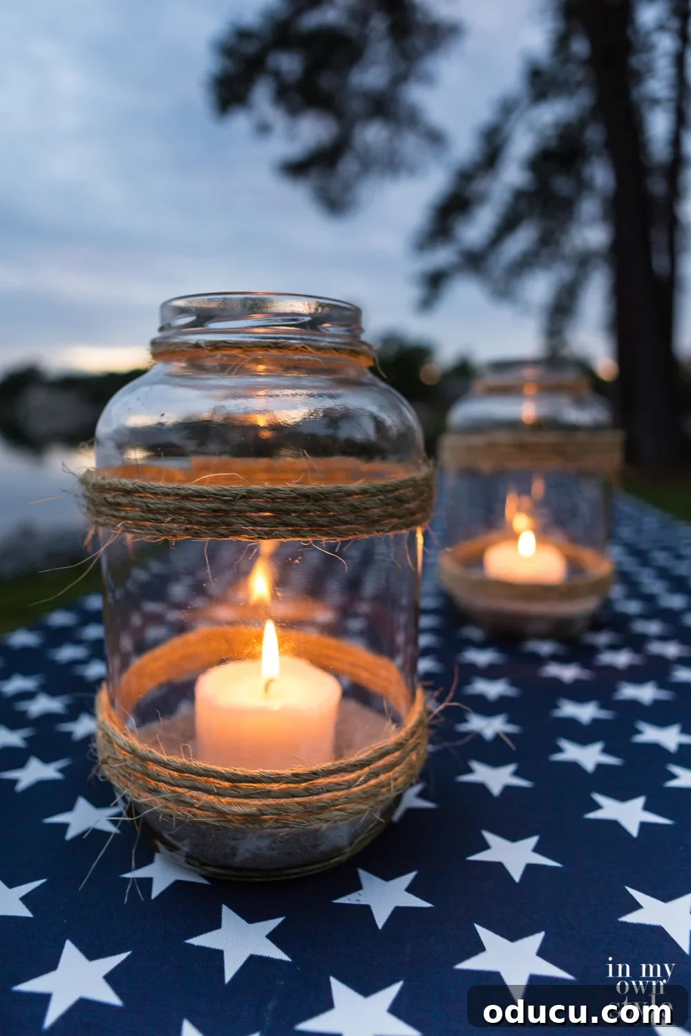 Craft a Stunning Oversized Glass Candle Lantern 3 Two DIY glass candle lanterns made in a nautical style, displayed on a white star and navy tablecloth, perfect for lakeside decor.