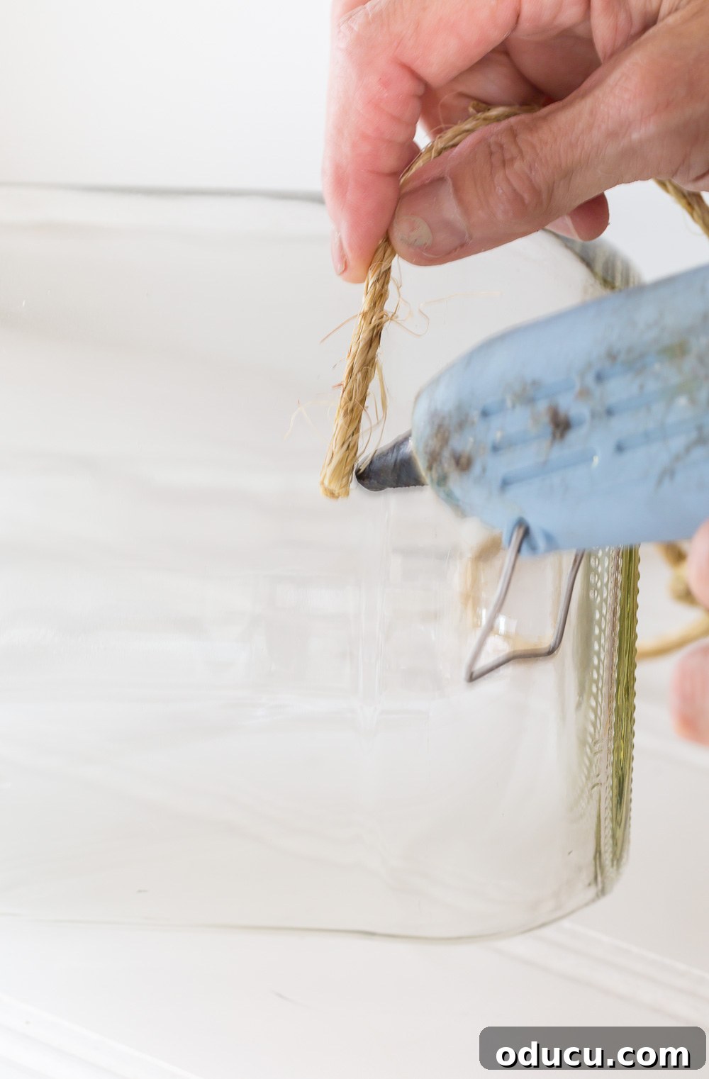 Craft a Stunning Oversized Glass Candle Lantern 6 Detailed image showing how to hot glue twine to a large glass pickle jar to create an outdoor table candle lantern.