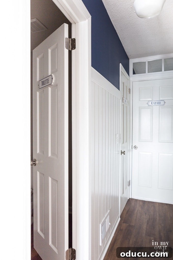 My Party Style Sanctuary 3 Long hallway featuring white doors and a deep navy wall above white paneling, awaiting decorative French enameled signs.