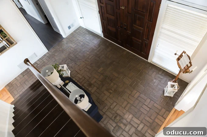 My $14 Whitewashed Brick Floor Makeover 4 Looking down from second floor of home onto a brown brick floor.