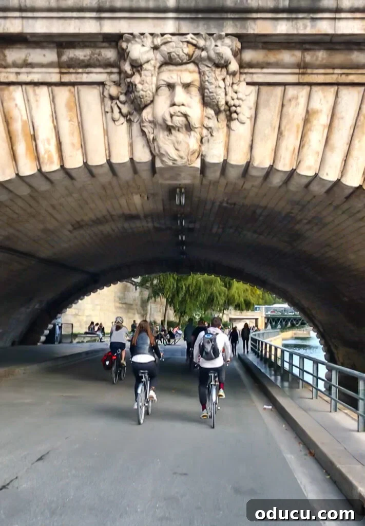 A group of cyclists on a Bike About Tours Paris tour, riding under a bridge along the scenic Seine River, enjoying the unique perspective.