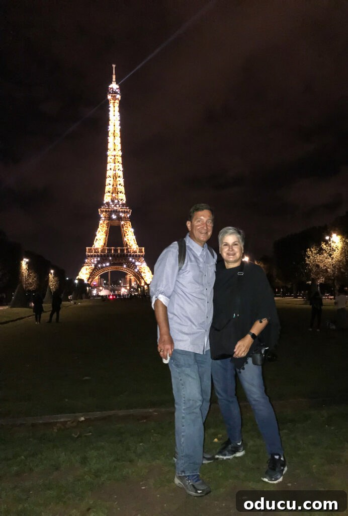 Blogger Diane Henkler and Ed proudly standing in front of the Eiffel Tower at night, sparkling and twinkling during their magical Paris bike tour adventure.