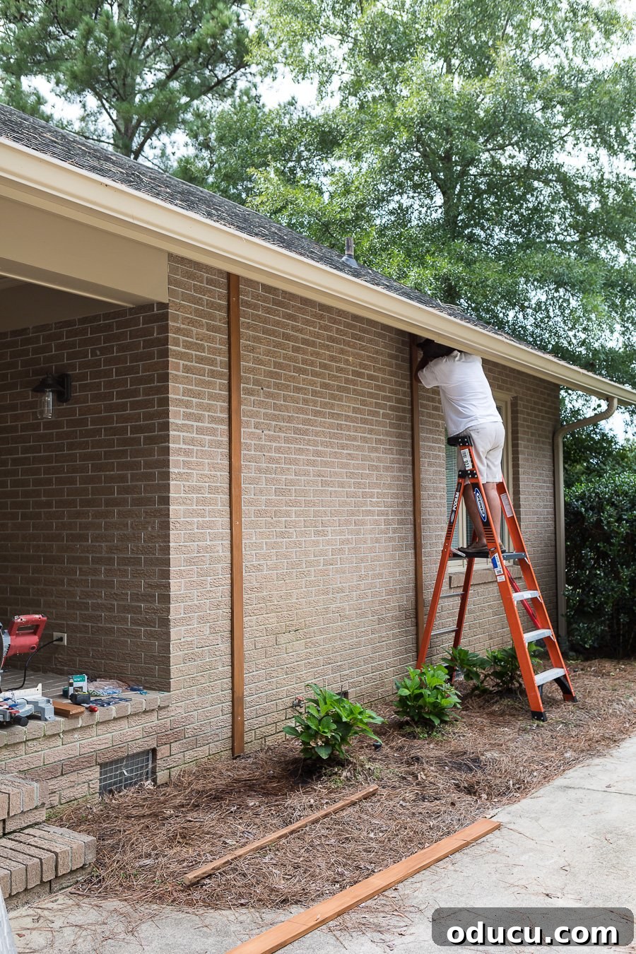 How to attach vertical wood boards to a brick wall to create a wood feature wall outdoor, showing careful alignment.