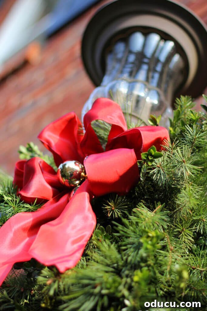 Outdoor light fixture on house with a red bow and greenery, showcasing simple yet elegant Christmas outdoor decorations