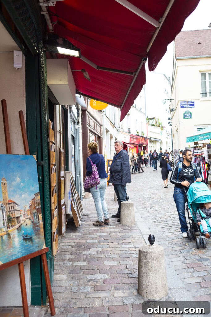 Ascending Paris's Masterpiece 13 Vibrant art displayed for sale along a charming cobblestone street in Paris, characteristic of the Montmartre area.