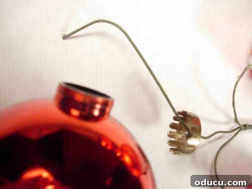 How to hang tie Christmas ornaments together Detailed step-by-step image demonstrating how to secure a heavy-gauge wire into a Christmas ornament by bending the end, showing how to create durable ornament attachments for holiday decor.