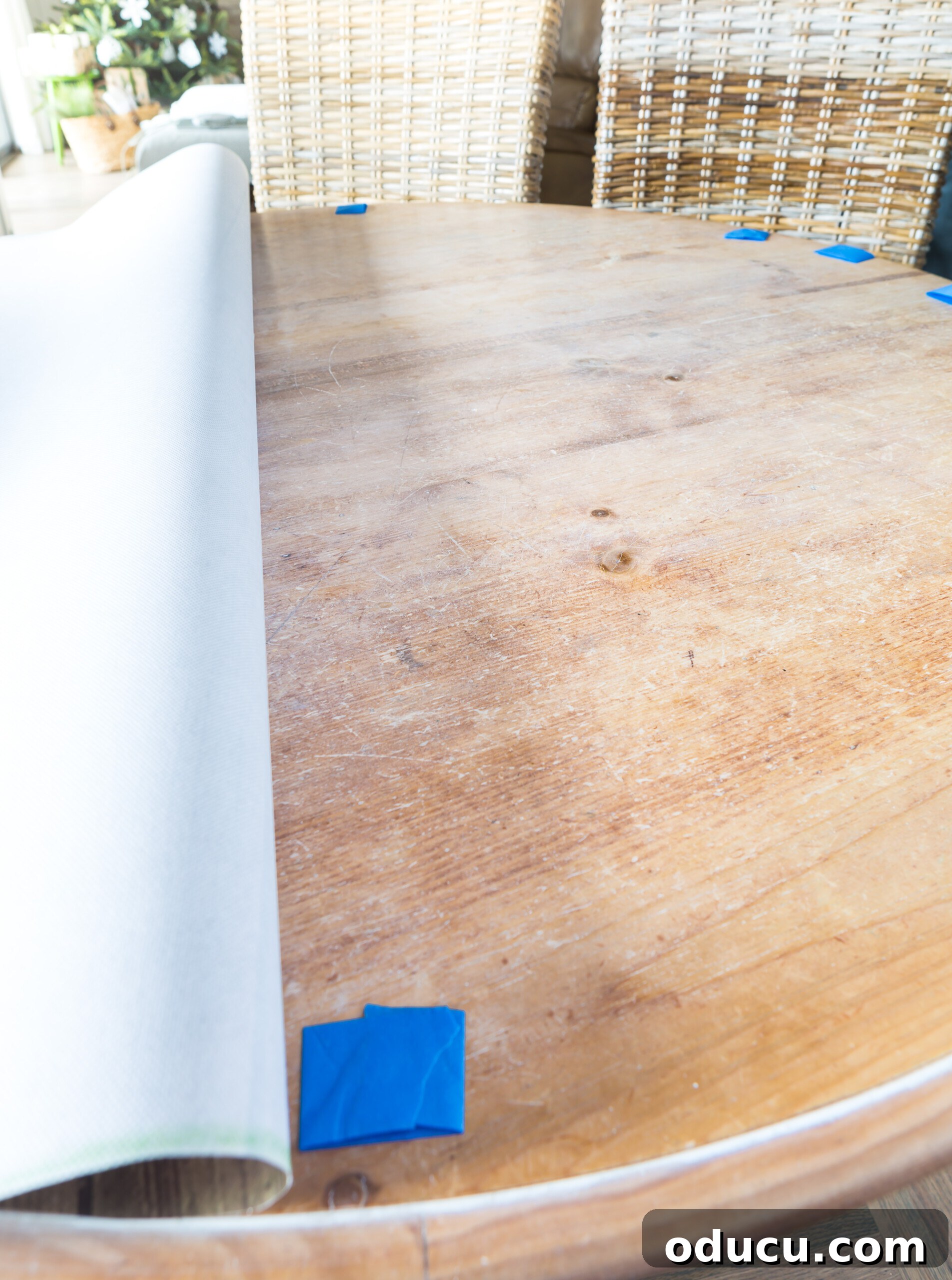 How to attach bulletin board roll to a dining table as a creative alternative to a cloth table cloth, illustrating the method of securing with tape rolls.