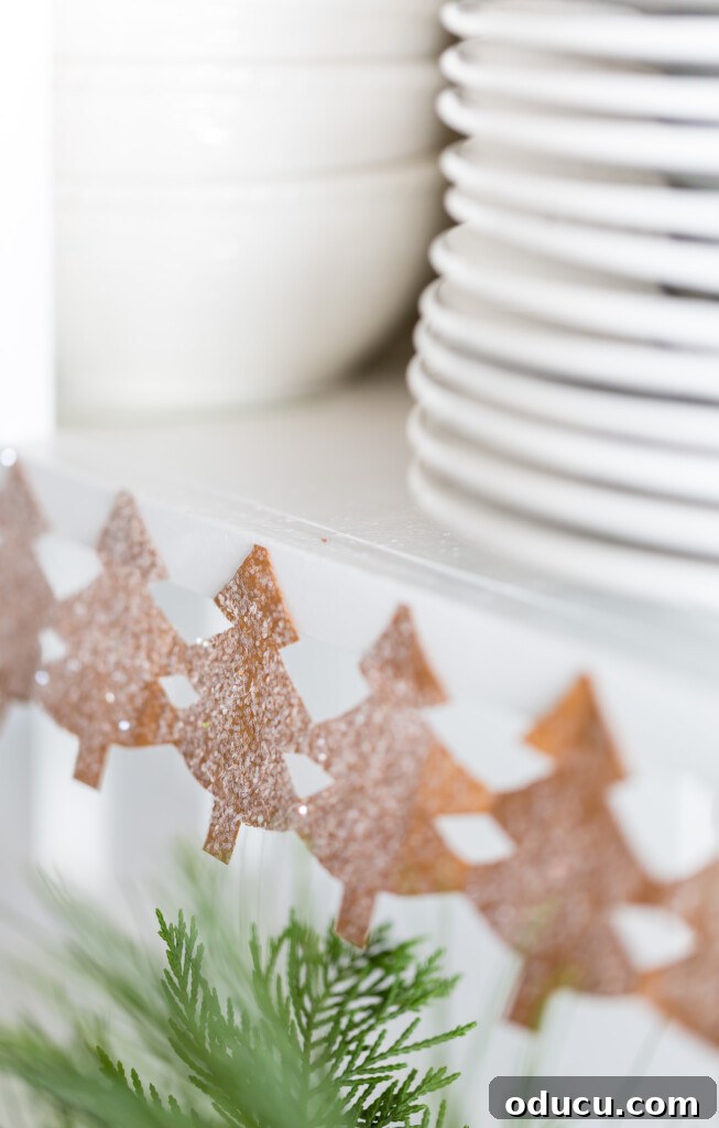 Craft Your Own Christmas Tree Paper Chain 7 Close up image of a paper chain of pine trees decorating the edge of kitchen shelves for the holidays.