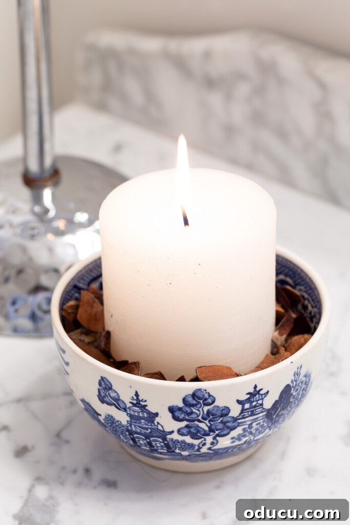 Quick Christmas Home Decor Hacks When Time is Tight 8 White candle in a bed of pine cone needles in.a blue and white bowl.