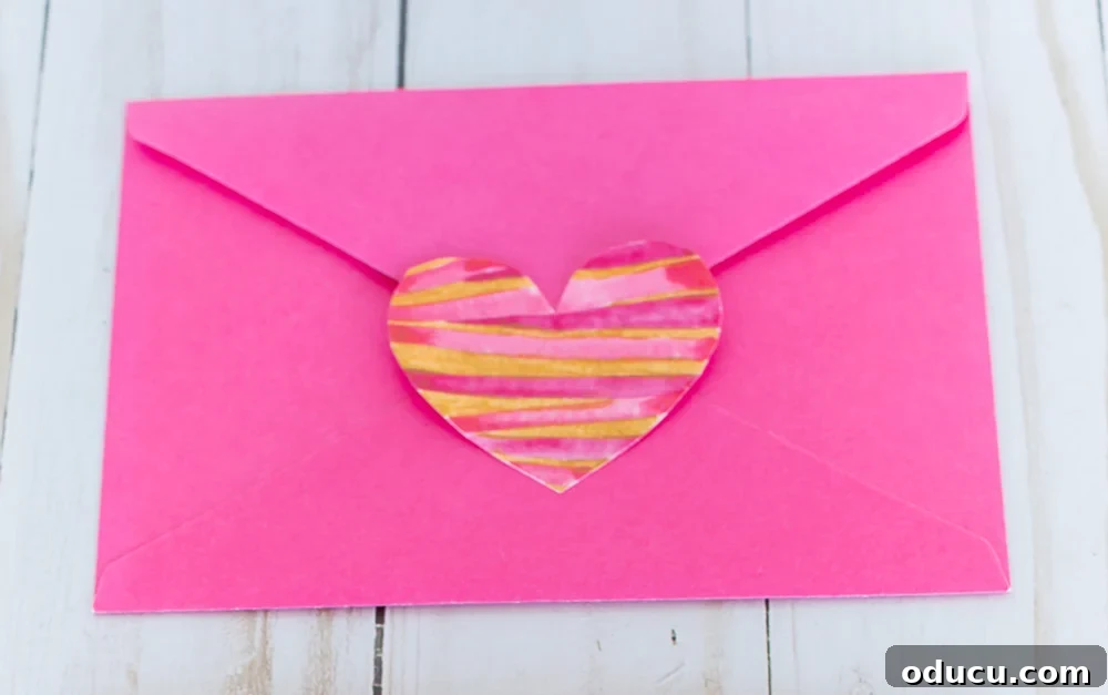 Valentine heart paper cutout glued to the flap of a pink envelope.