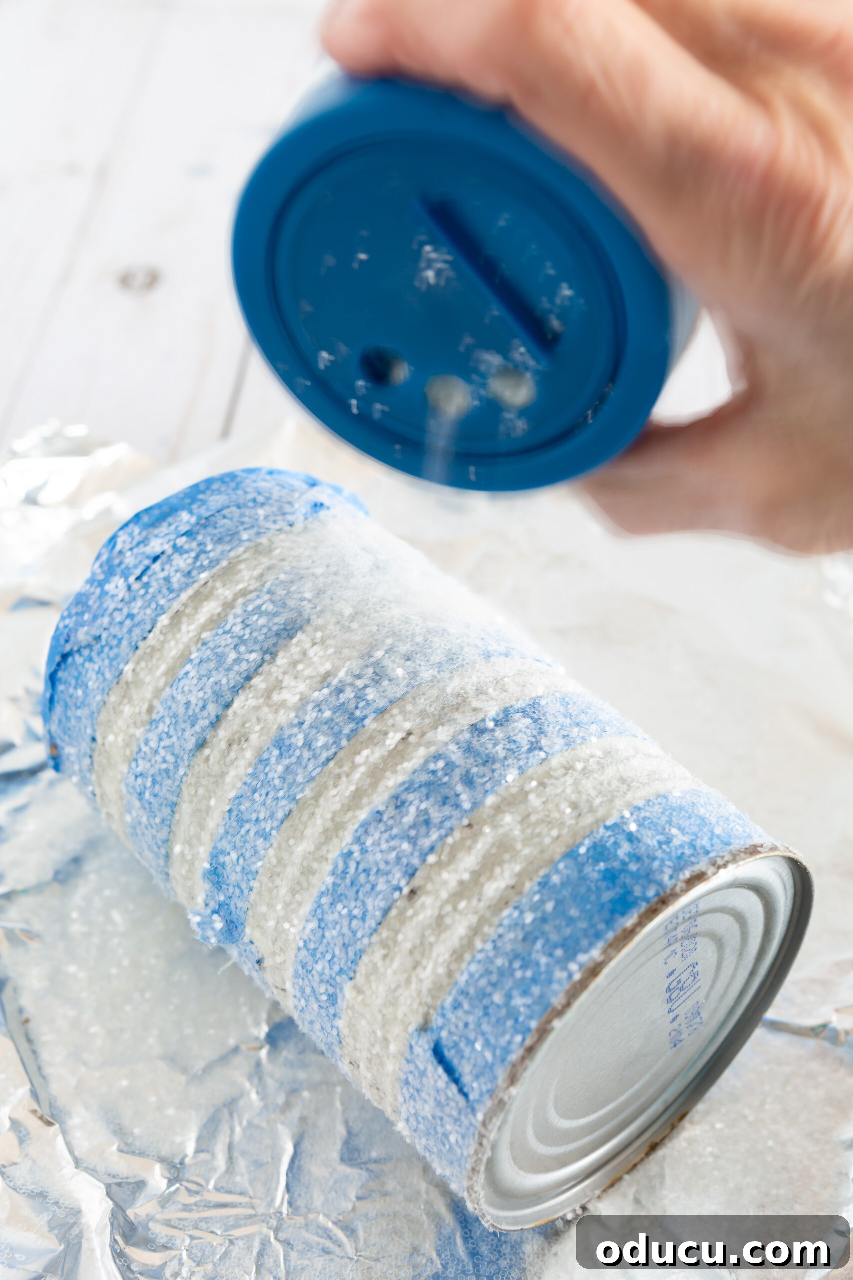 applying glitter to a tin can to make a pretty vase or centerpiece on a budget