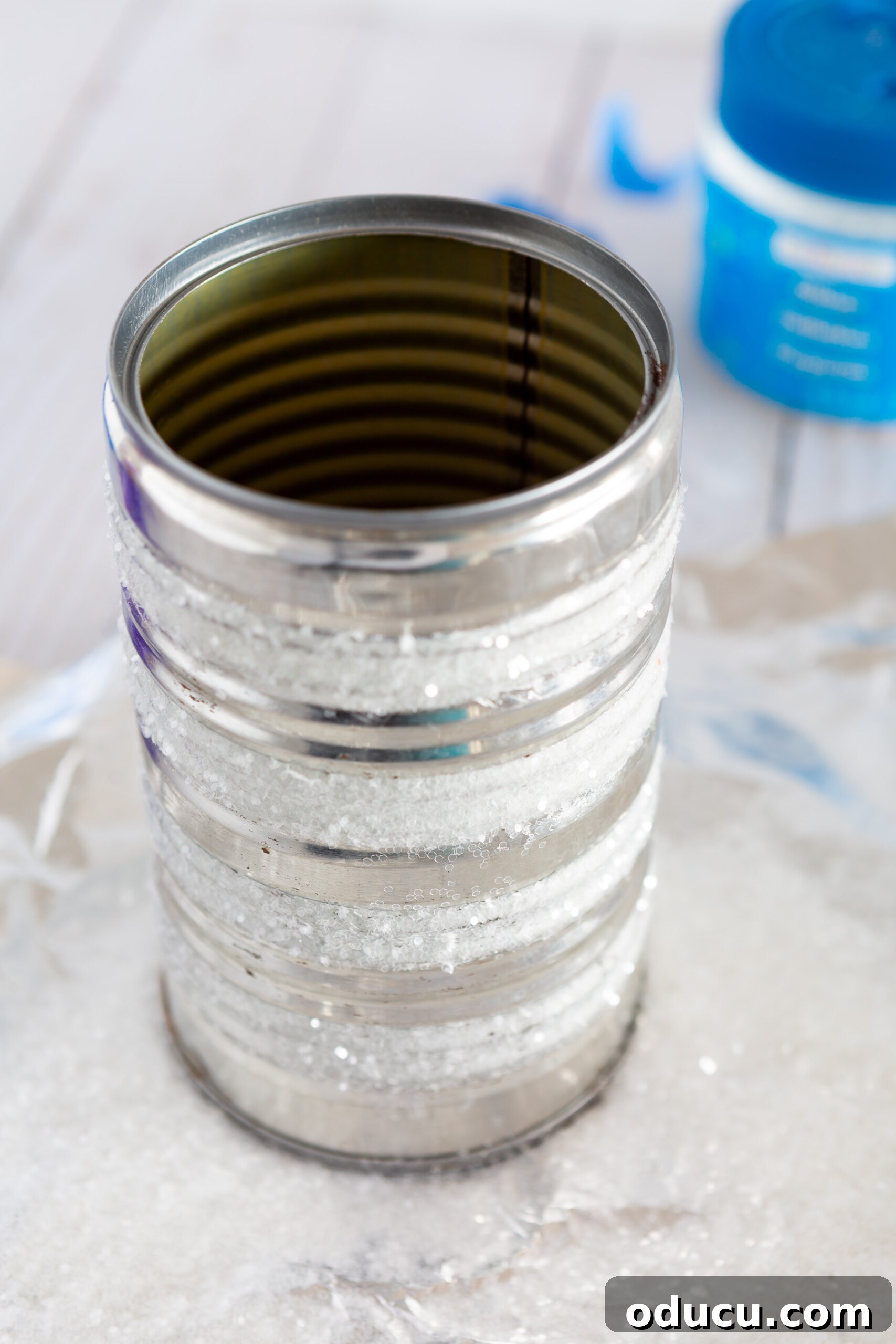 how to steps showing how to add stripes of glitter on a tin can to make a pretty vase for a kitchen counter.