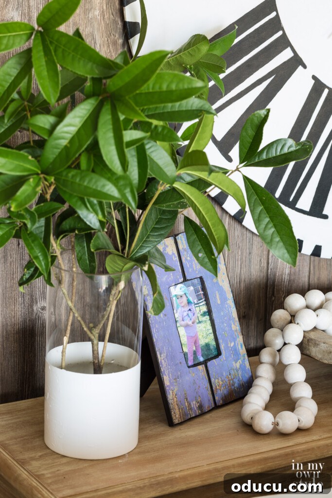 Effortless Summer Style 7 Summer decorating ideas for a sofa table. Green clippings from shrubs in glass and white vase next to purple photo frame and wood beads on a table.